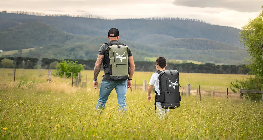 Father and son hiking through long grass with Bushlads packs
