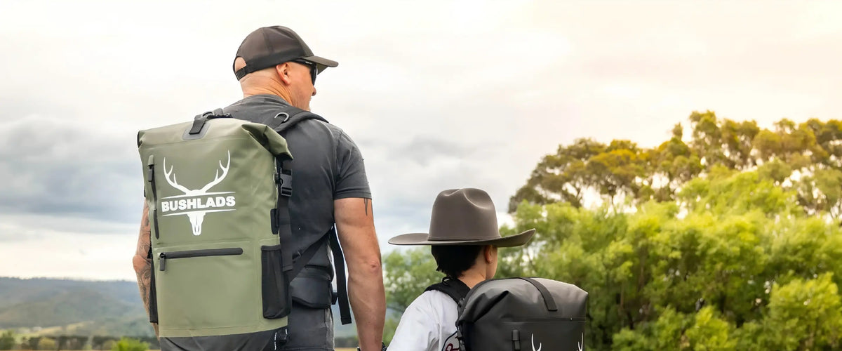 Man wearing the olive Bushlads 35L backpack walking a bush track with a boy in a black daypack