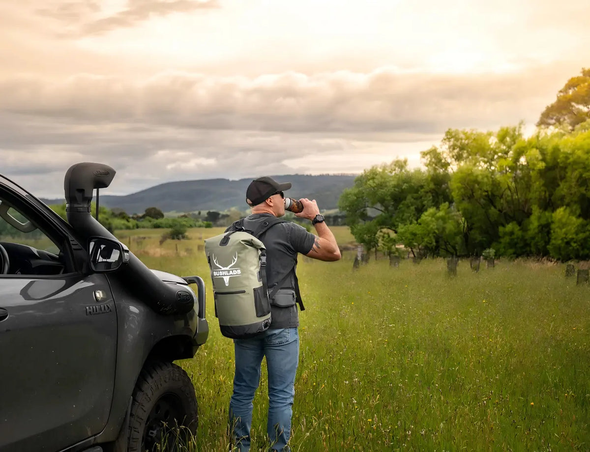 Man loading the Bushlads 35L backpack beside a 4WD in open grassland at sunset