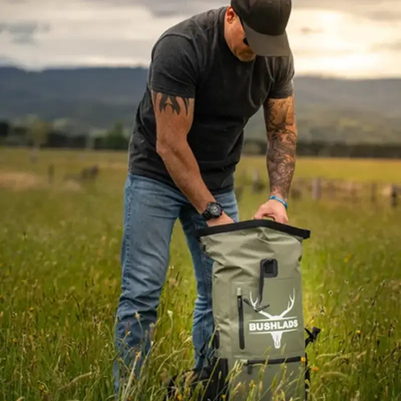Man opening the roll-top of the Bushlads 35L backpack in an open field